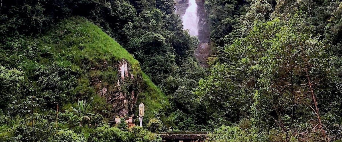 A waterfall cascading down a lush, green hillside surrounded by dense forest.