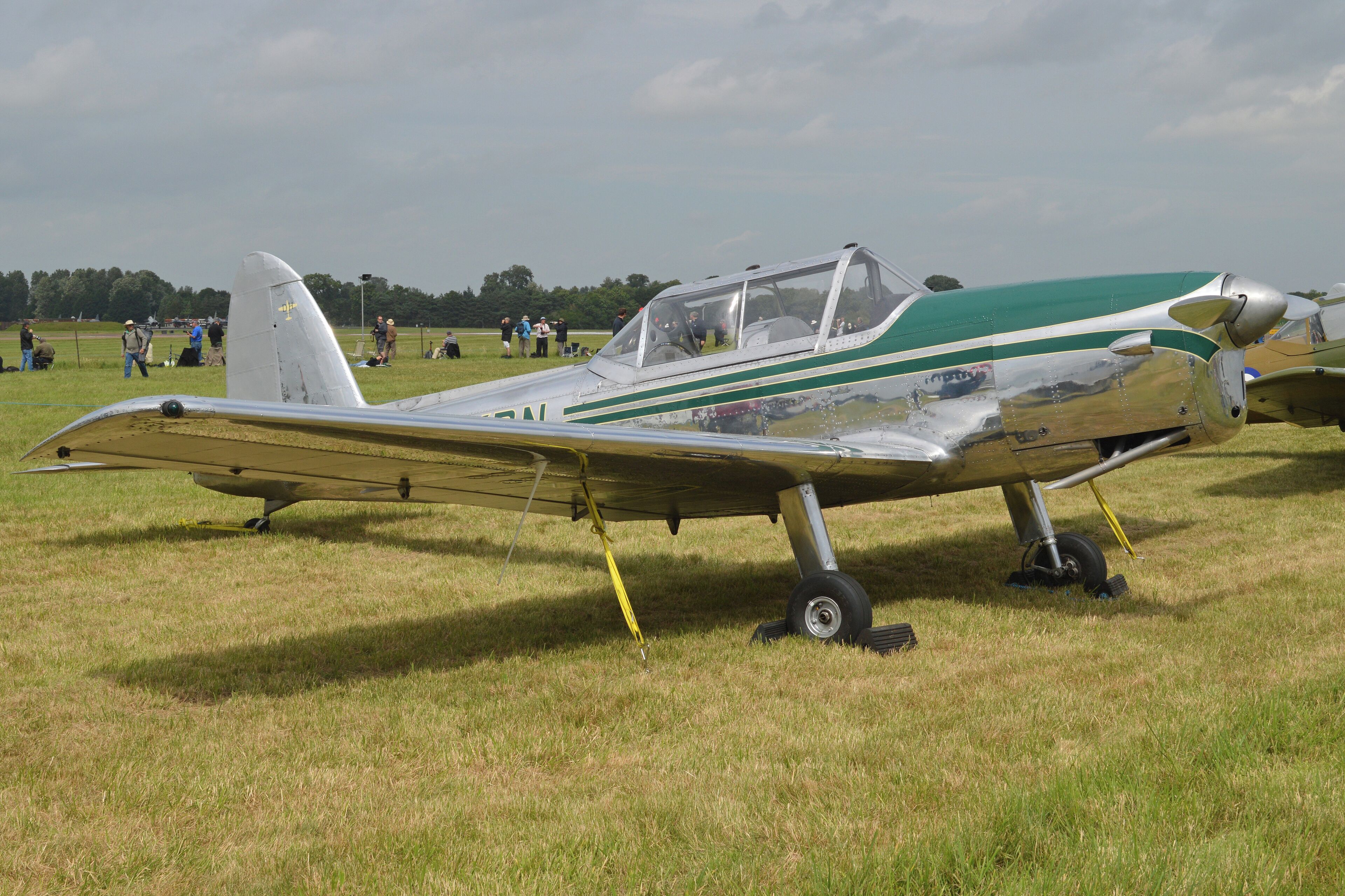 A vintage aircraft with a green and white color scheme parked on a grassy field.