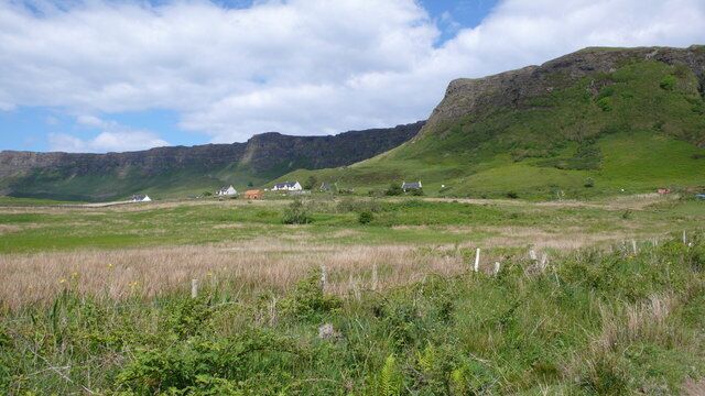 A grassy field with a few white buildings and a mountain in the background.