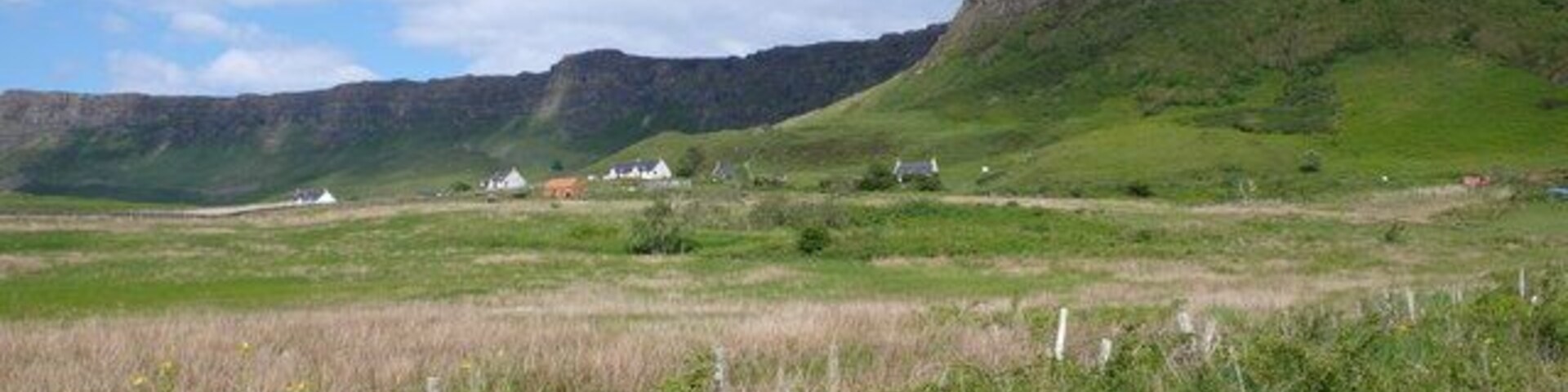 A grassy field with a few white buildings and a mountain in the background.