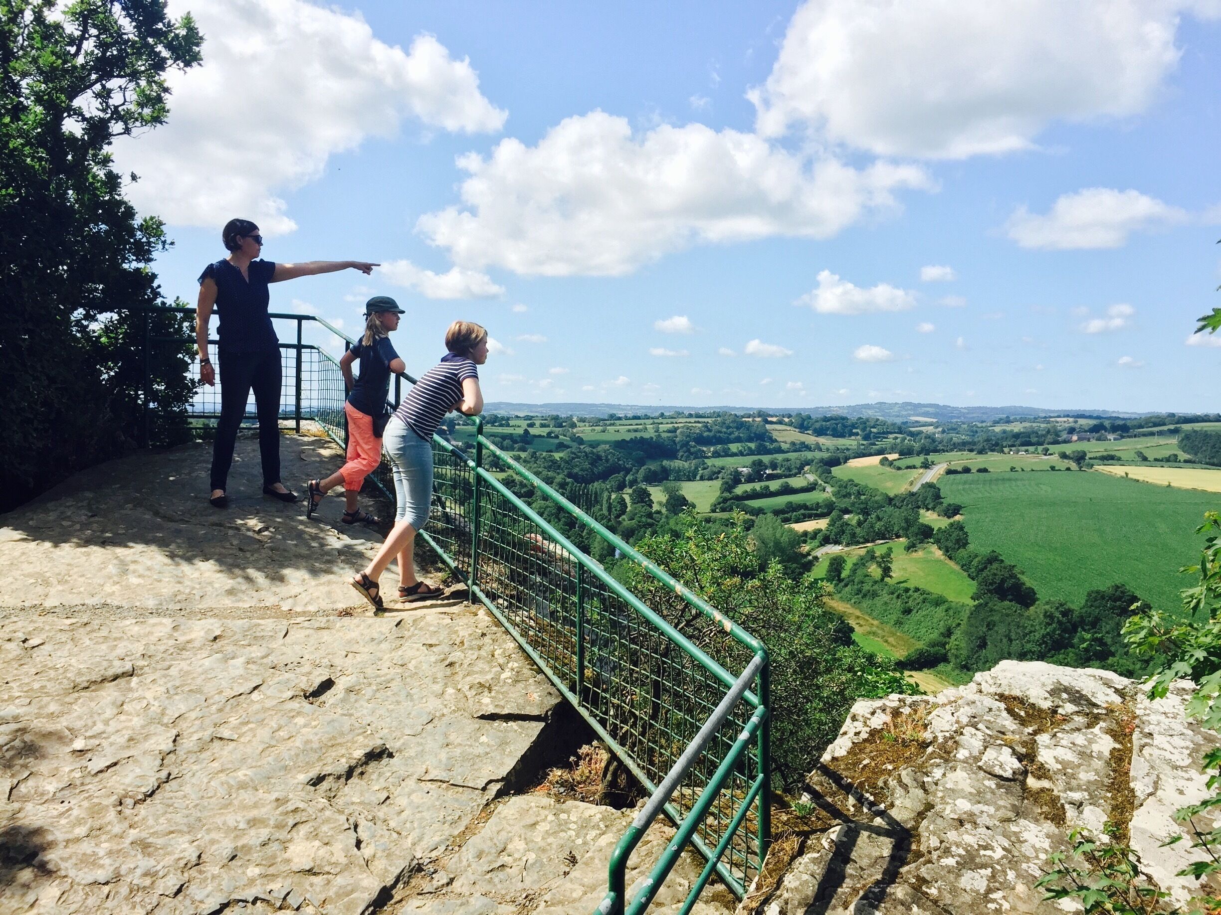 A group of people on a stone platform overlooking a green valley with a clear sky.