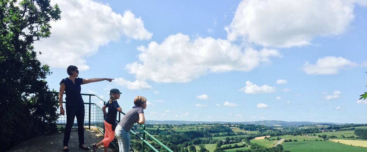 A group of people on a stone platform overlooking a green valley with a clear sky.