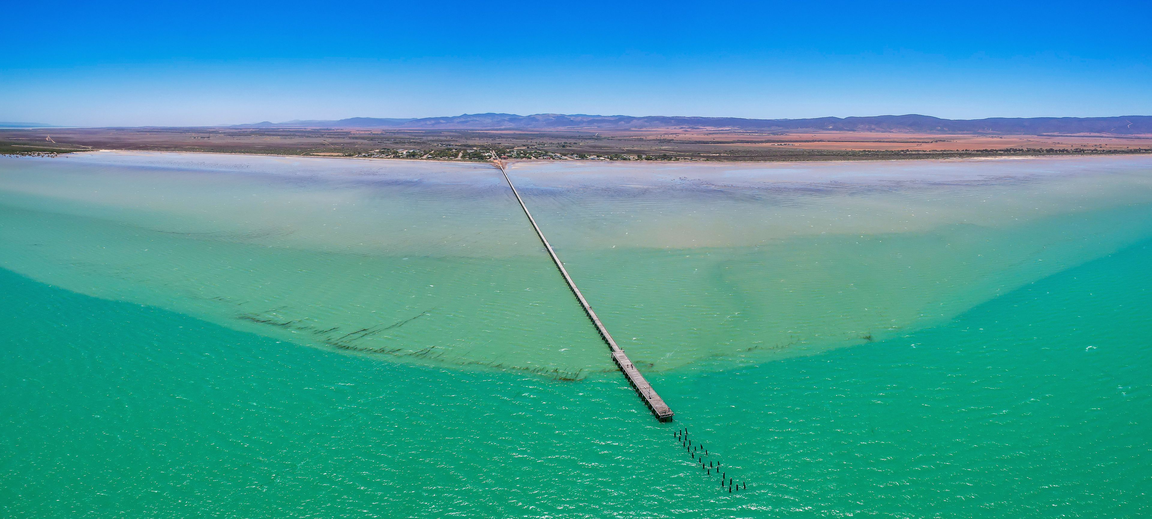 Aerial view of tranquil Germein Bay with a long straight jetty under a clear blue sky, Port Germein, Australia.