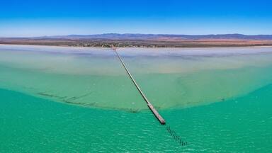 Aerial view of tranquil Germein Bay with a long straight jetty under a clear blue sky, Port Germein, Australia.