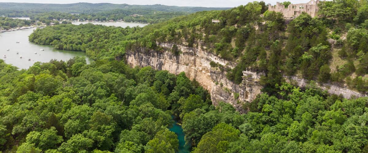 A lush green valley with a river, a cliff with a castle, and distant mountains.