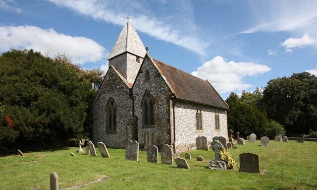 A stone church with a pointed steeple and a graveyard in front.