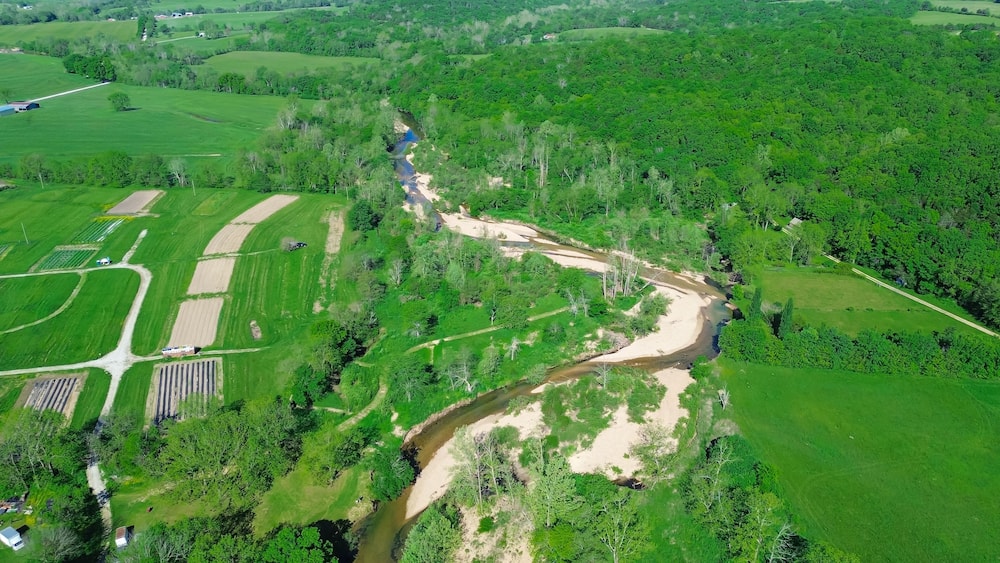 Acres of farmland with curved Lick Fork Gasconade River sandy bank running water moving to lower level in Wright County, Mansfield, Missouri, lush greenery Ozark, scenic countryside rural aerial