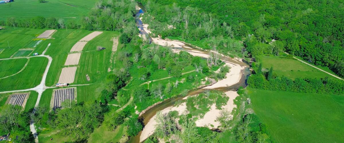 Acres of farmland with curved Lick Fork Gasconade River sandy bank running water moving to lower level in Wright County, Mansfield, Missouri, lush greenery Ozark, scenic countryside rural aerial