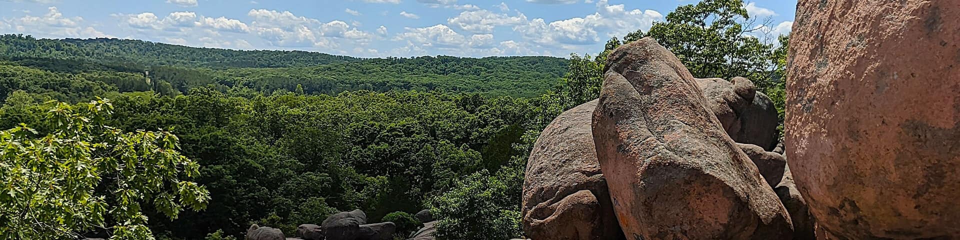A rocky landscape with large boulders and a forested hill in the background.