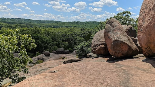 A rocky landscape with large boulders and a forested hill in the background.