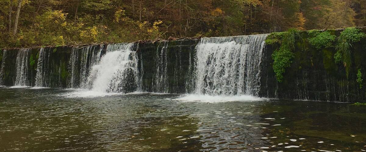 A waterfall cascading over a rocky ledge surrounded by autumn-colored trees.