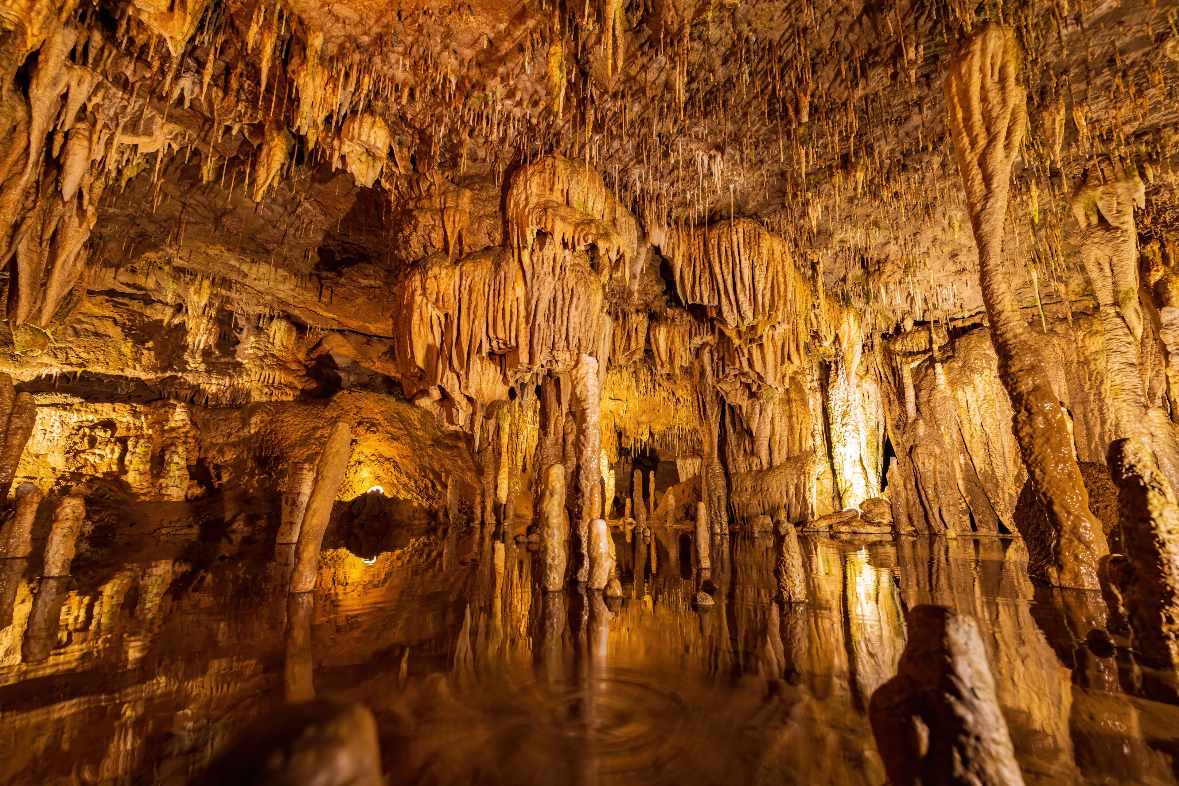 Une grotte ornée de stalactites et de stalagmites, où l’on peut admirer les reflets de l’eau et observer l’ouverture de la grotte.