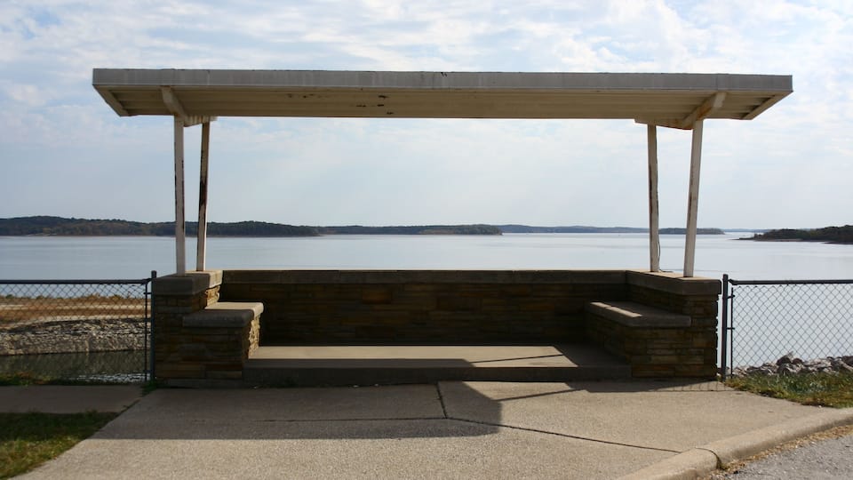 A concrete bench with a roof overlooking a body of water.