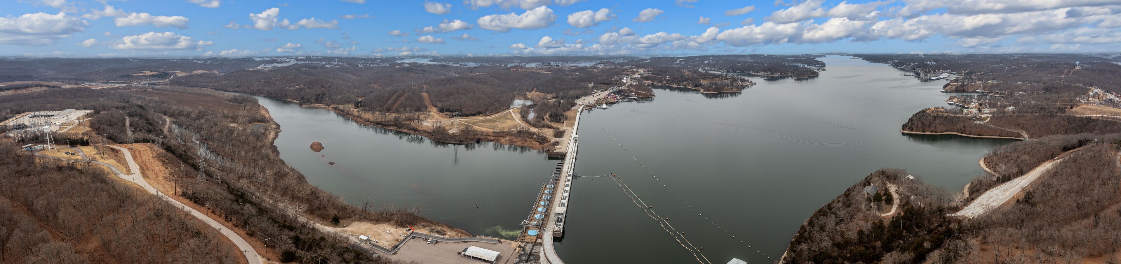 A river with a bridge, surrounded by forested hills and a distant city skyline.