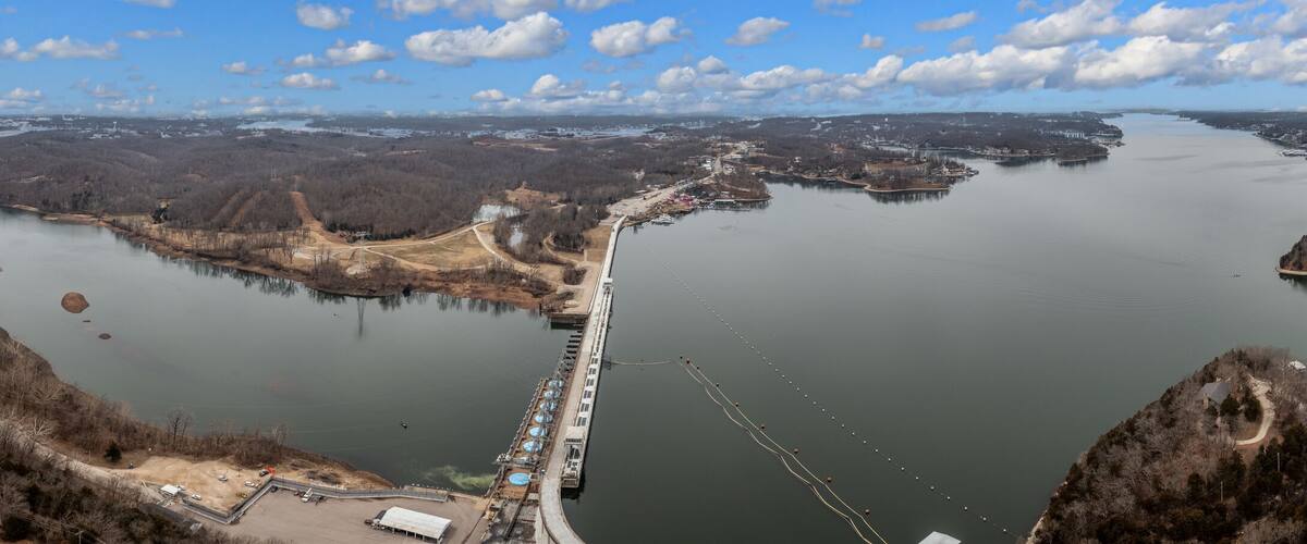 A river with a bridge, surrounded by forested hills and a distant city skyline.