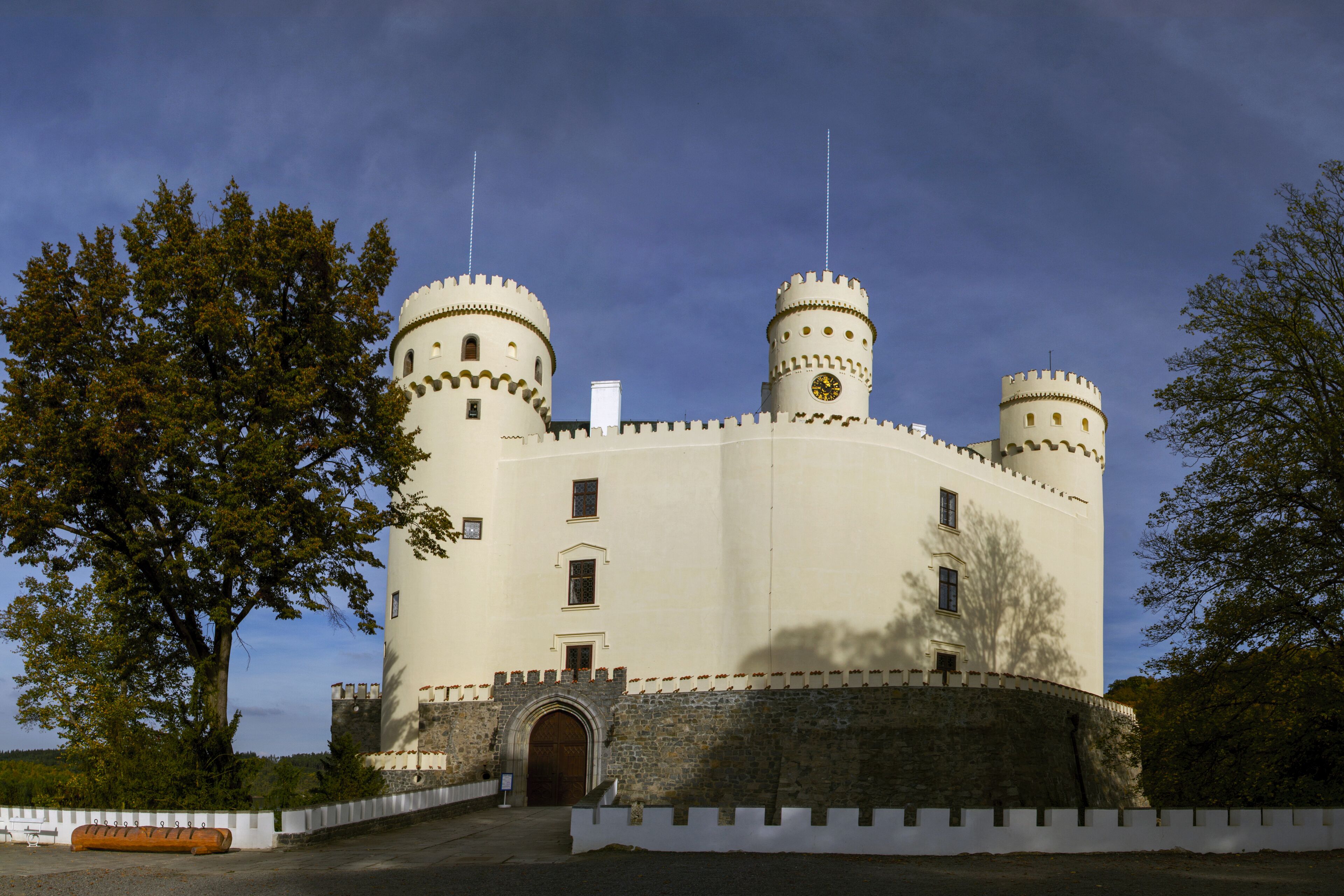 A castle with two towers, a large arched entrance, and a white wall with battlements.