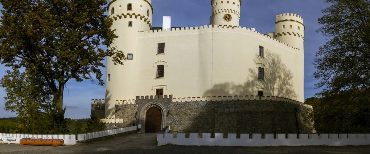 A castle with two towers, a large arched entrance, and a white wall with battlements.