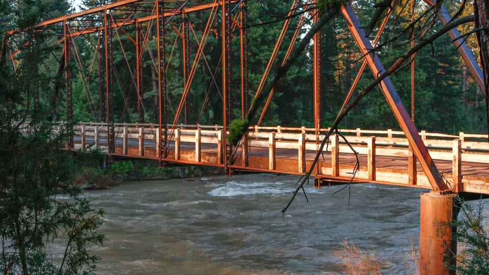 A metal bridge over a river surrounded by trees.