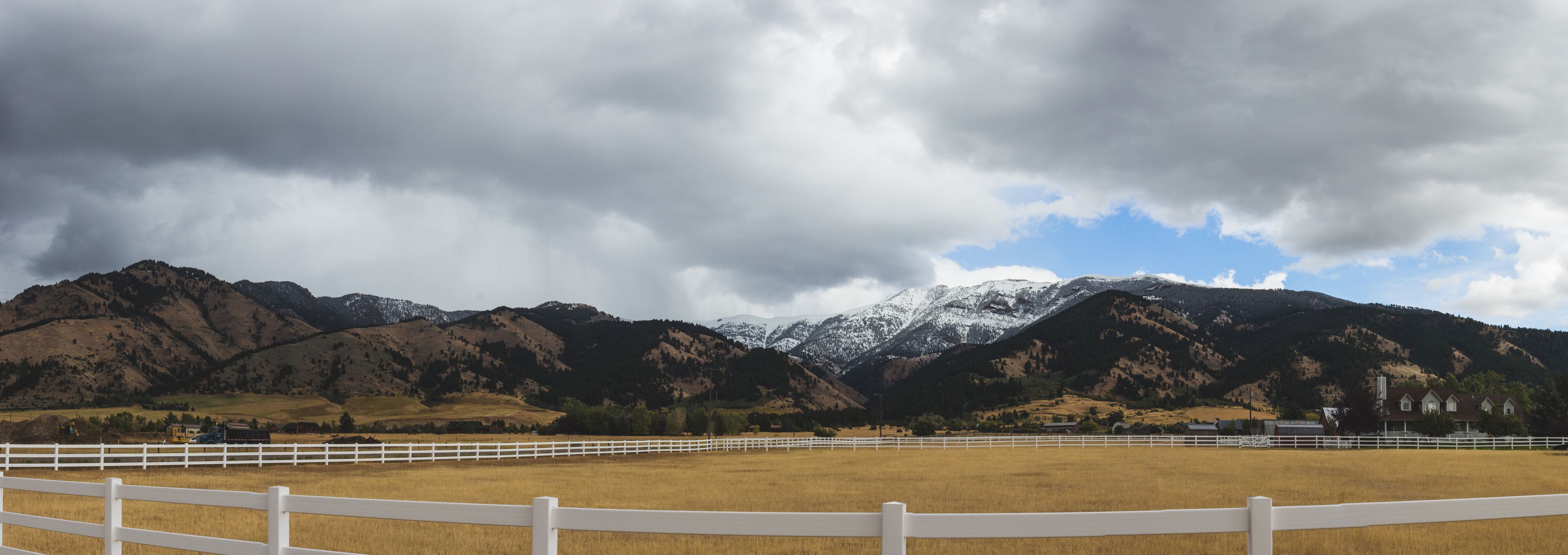 A mountainous landscape with a white fence in the foreground and a cloudy sky.