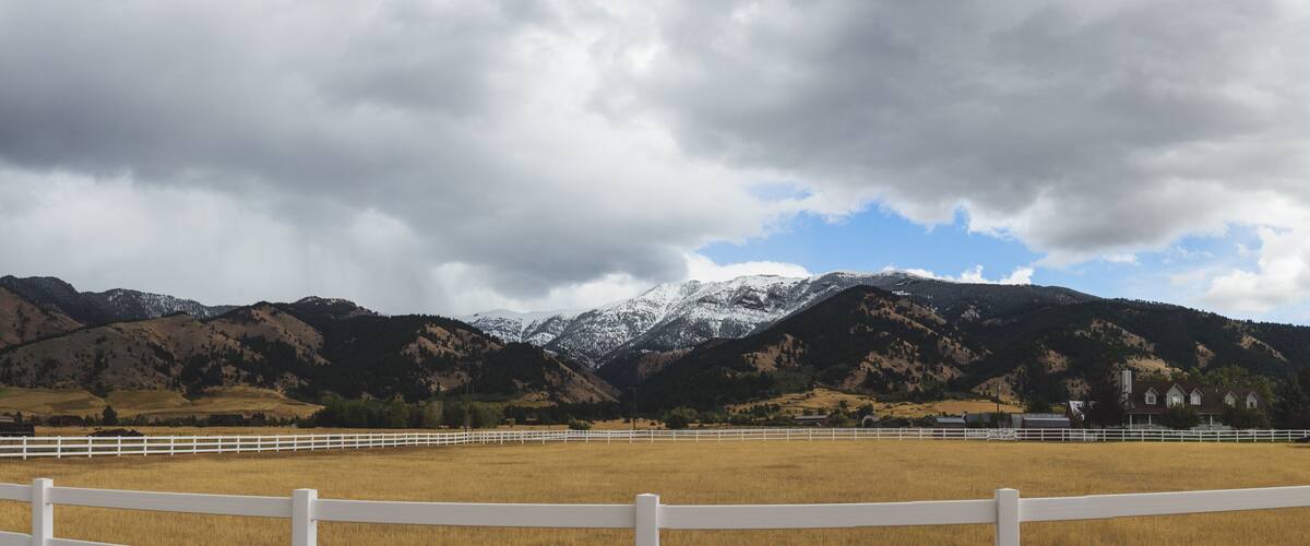 A mountainous landscape with a white fence in the foreground and a cloudy sky.