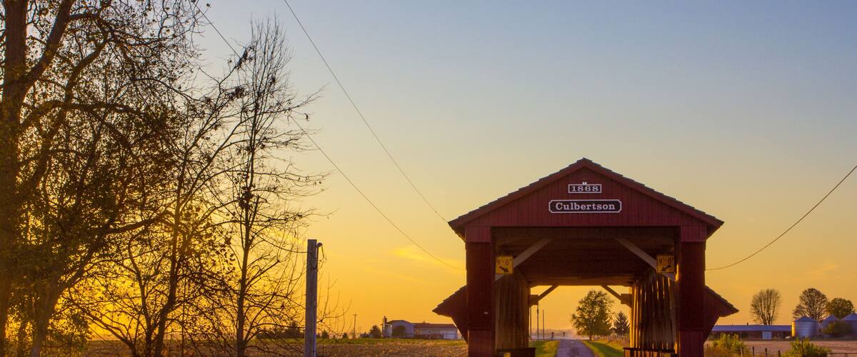A covered bridge with a sign reading "Cumberland" and a sunset in the background.
