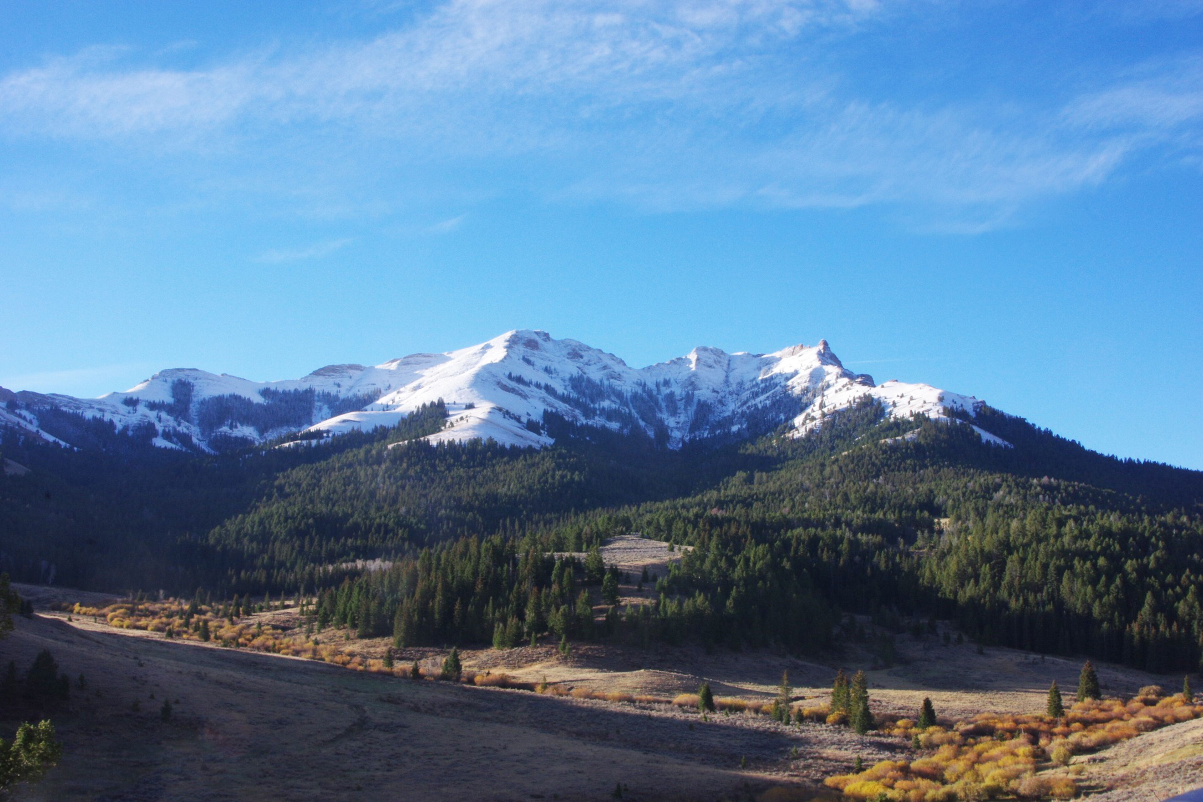 A mountain range with snow-capped peaks, a valley with autumn-colored foliage, and a clear blue sky.