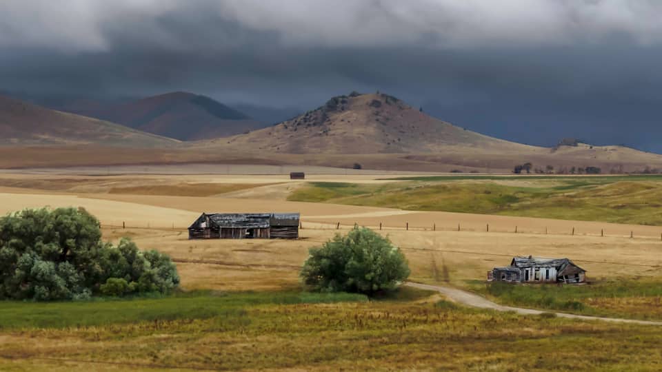 A rural landscape with rolling hills, a barn, and a dirt road.