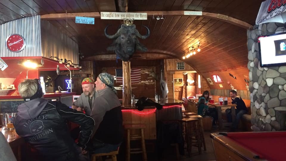 A bar with wooden walls, a clock, and a sign that says "Be careful how you address the Queen."