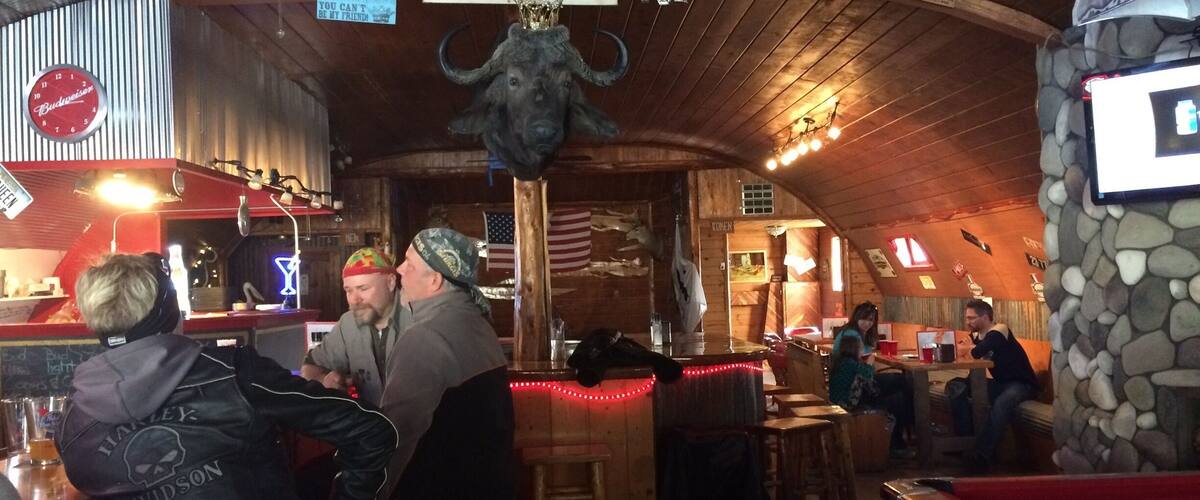 A bar with wooden walls, a clock, and a sign that says "Be careful how you address the Queen."