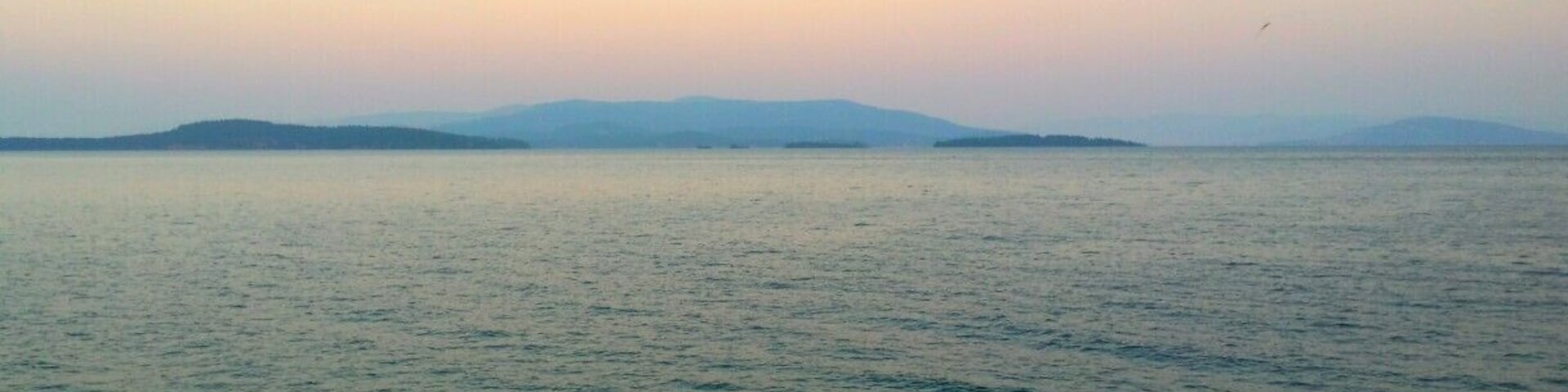 A calm sea with distant landforms under a clear sky.