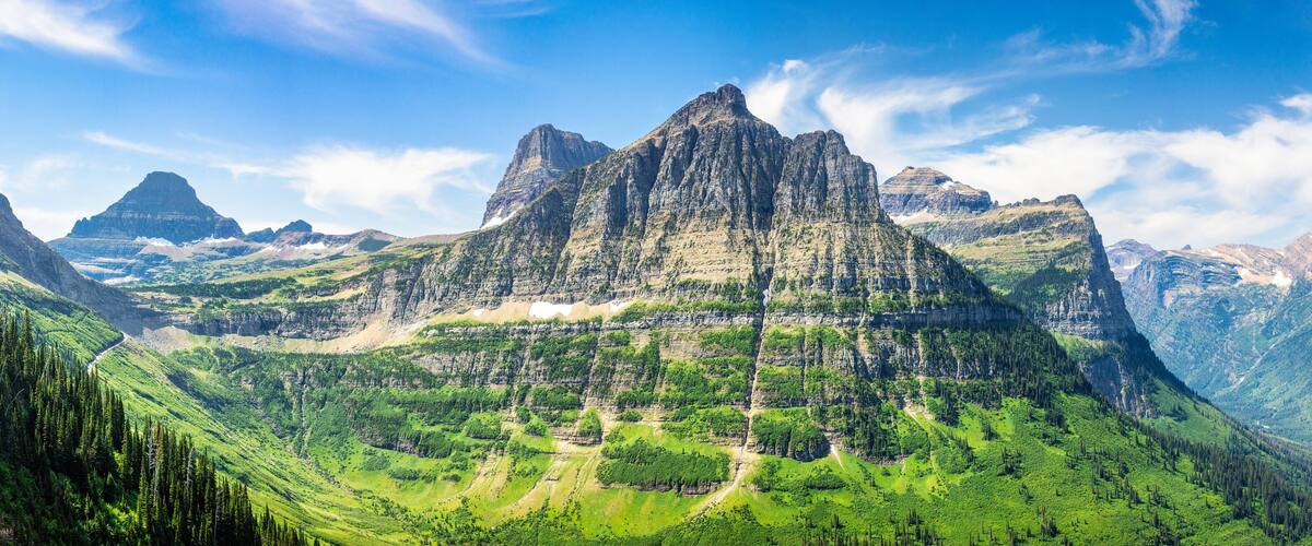 A mountain range with a prominent peak, lush green valleys, and a clear blue sky.