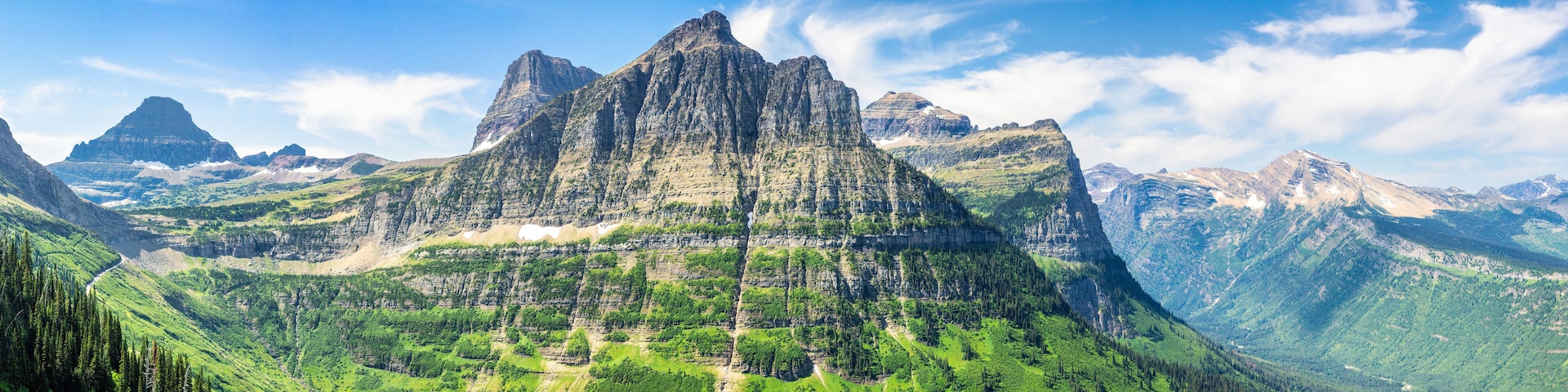 A mountain range with a prominent peak, lush green valleys, and a clear blue sky.