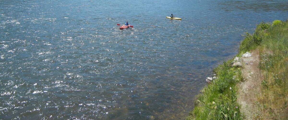 A river with kayakers, surrounded by green hills and a clear sky.