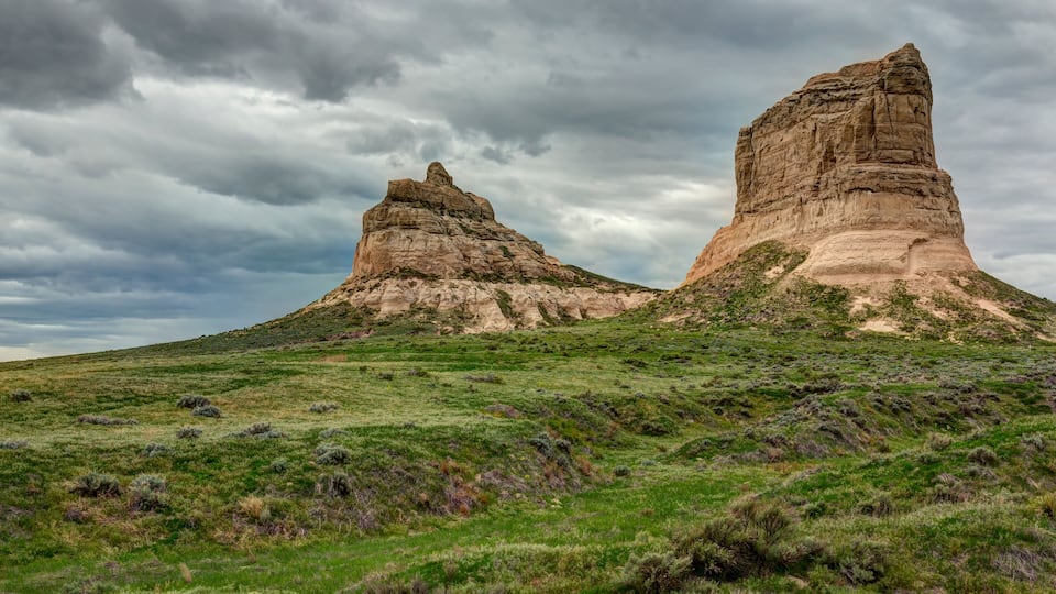A landscape with two prominent rock formations under a cloudy sky.