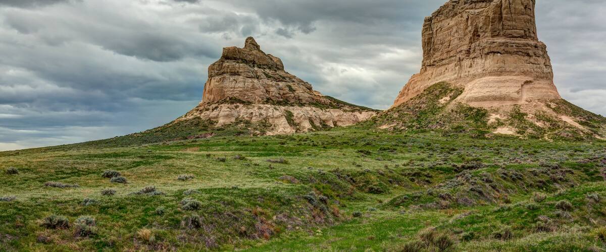 A landscape with two prominent rock formations under a cloudy sky.