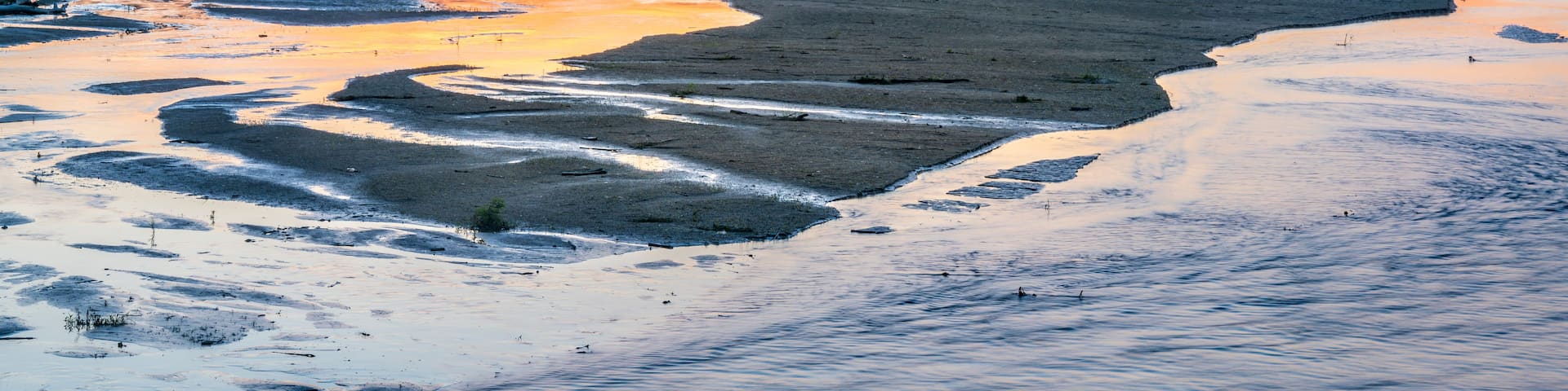 A river with a sandy bank and a sunset in the background.