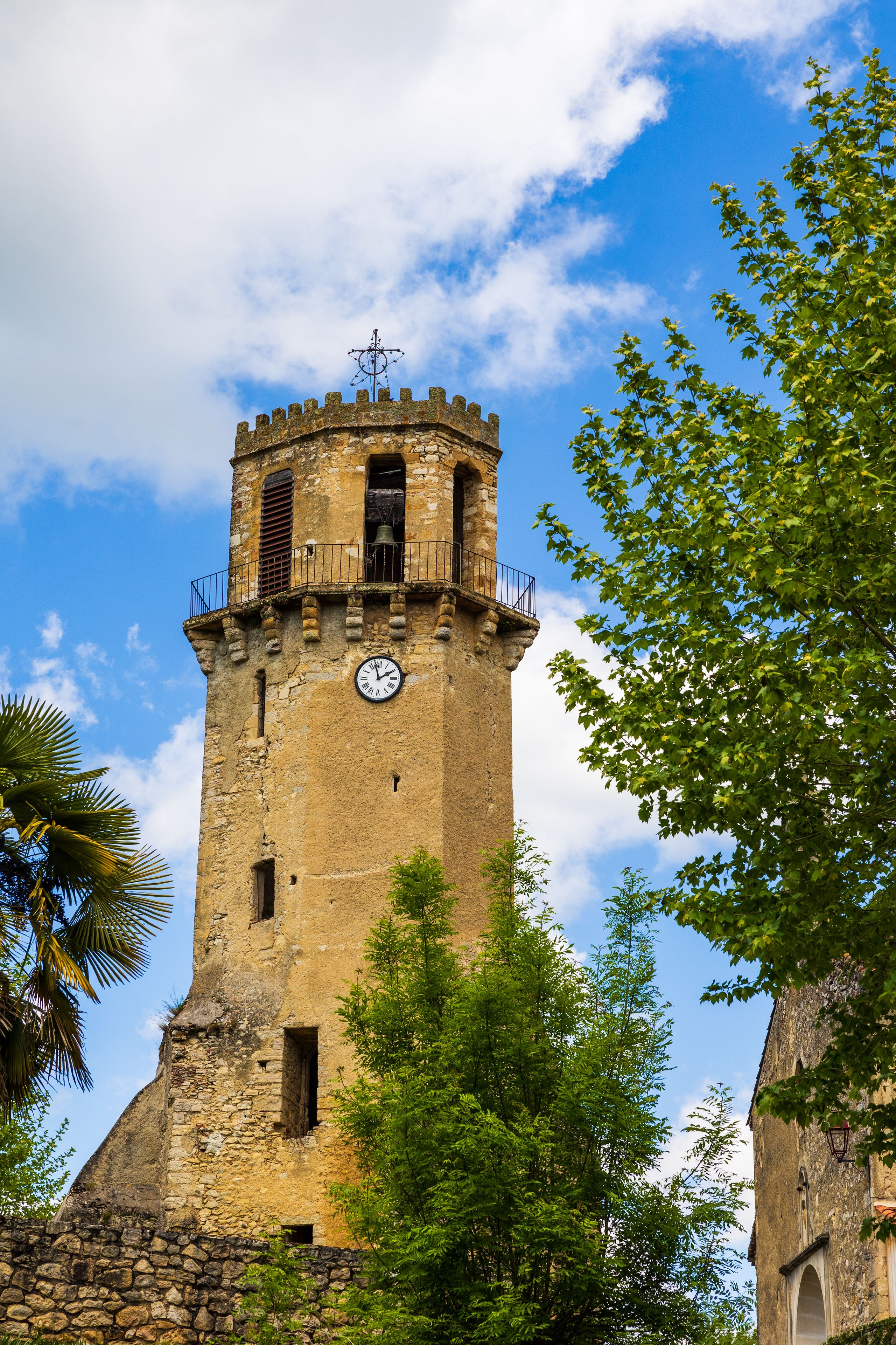 Une tour historique, dotée d’une horloge, entourée d’une végétation luxuriante et surplombant un ciel d’un bleu limpide.
