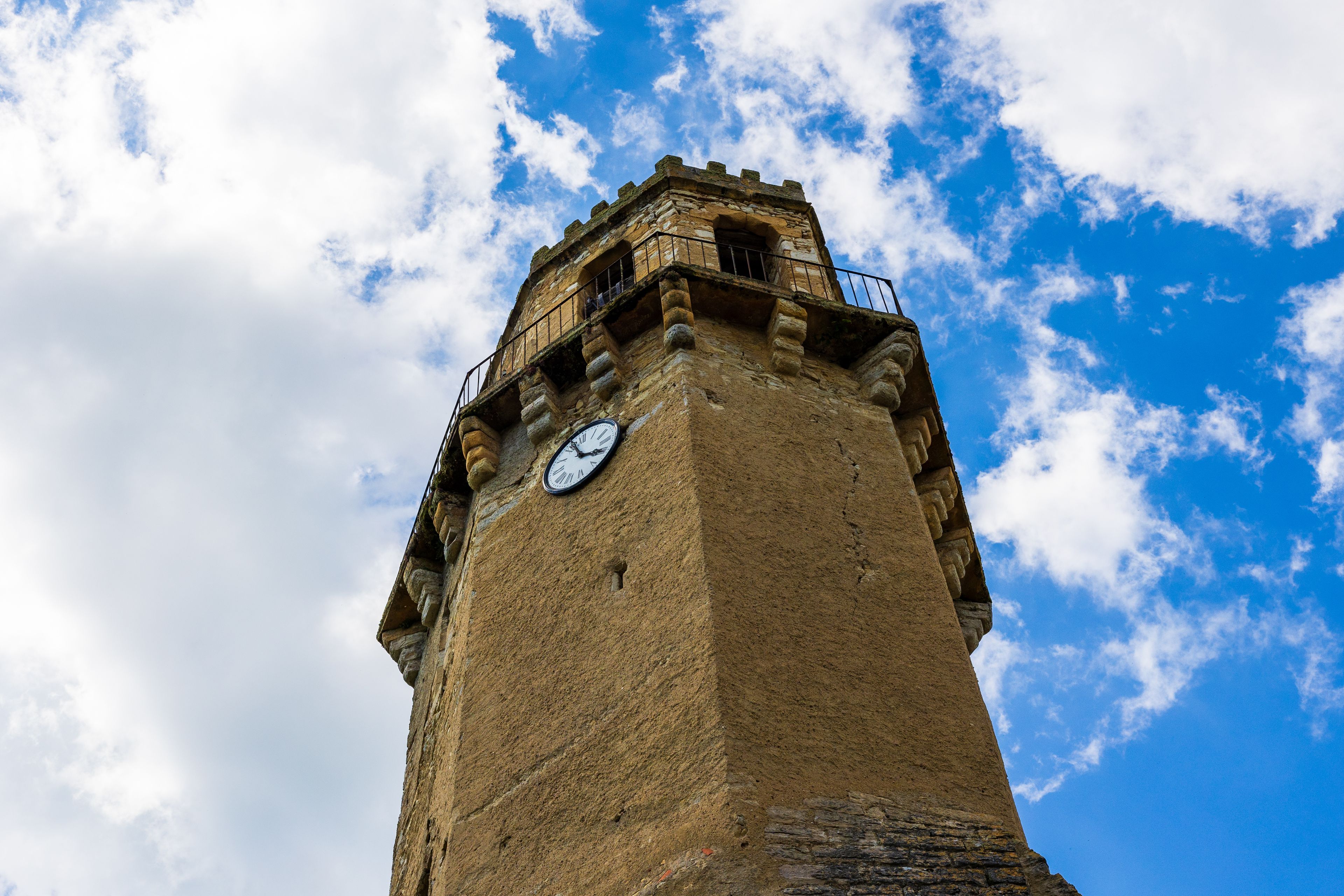 Une haute tour surmontée d’une horloge, se dressant sur un ciel partiellement nuageux.