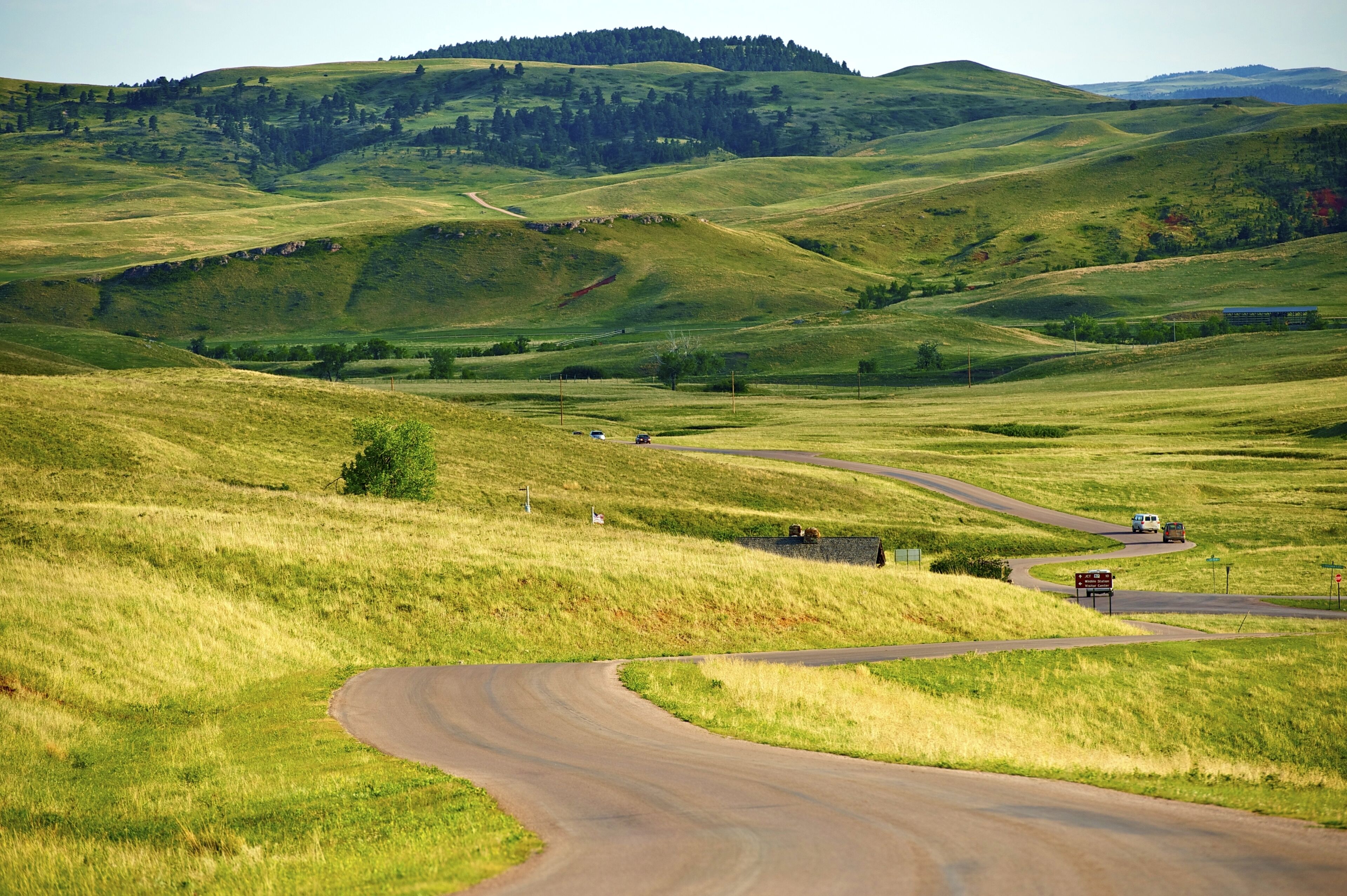 A winding road through rolling green hills with a small building and a signpost visible.