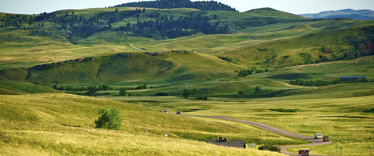A winding road through rolling green hills with a small building and a signpost visible.