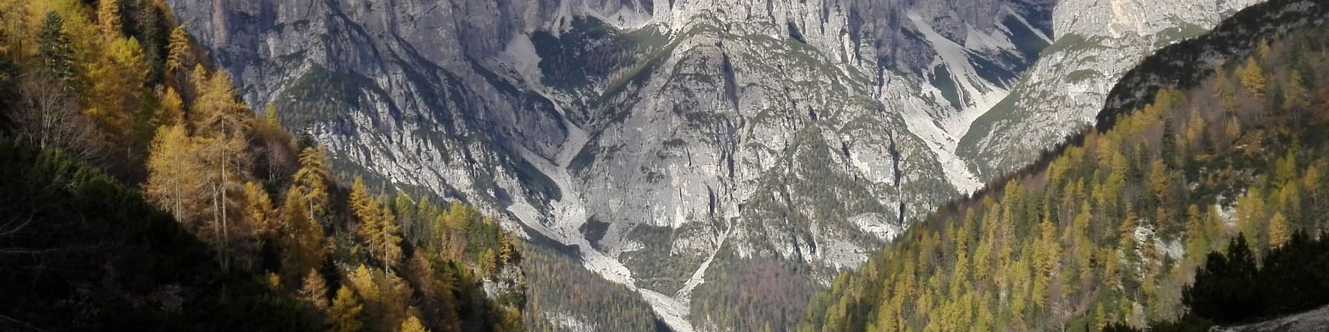 A mountainous landscape with rugged peaks, a valley, and autumn-colored trees.