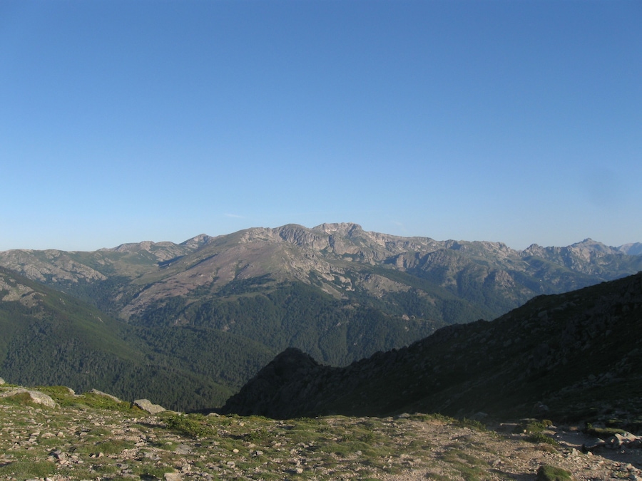 A mountain range with rocky peaks and forested valleys.