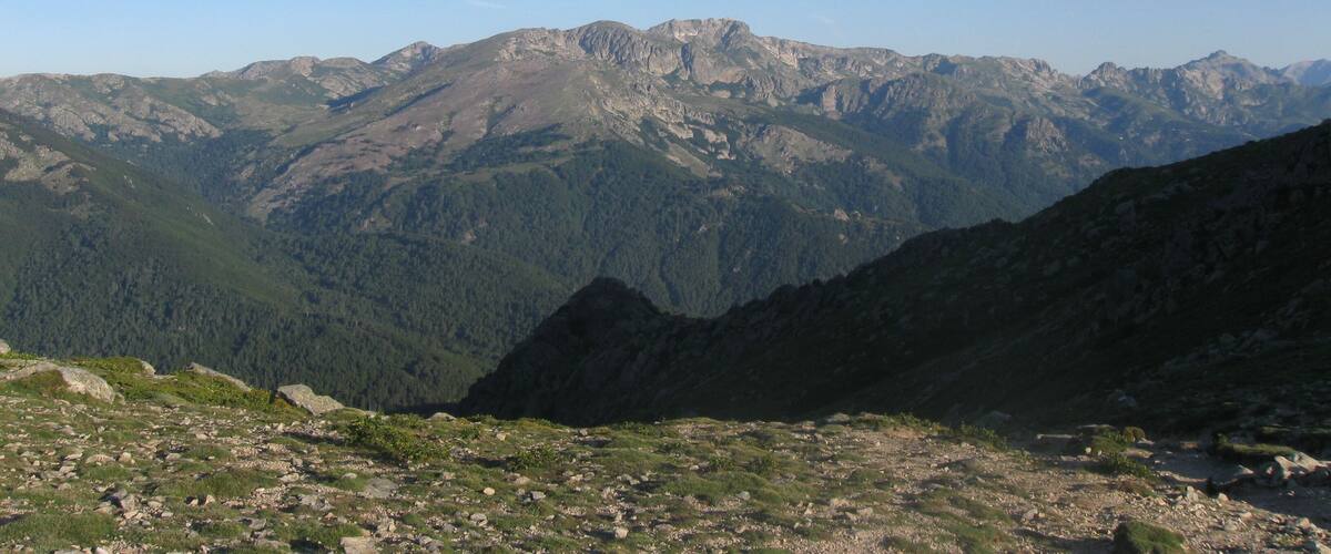 A mountain range with rocky peaks and forested valleys.