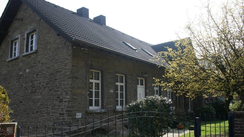 A stone house with a tiled roof, a metal fence, and a tree with yellow flowers.