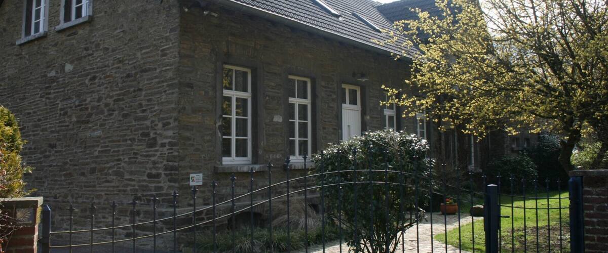 A stone house with a tiled roof, a metal fence, and a tree with yellow flowers.