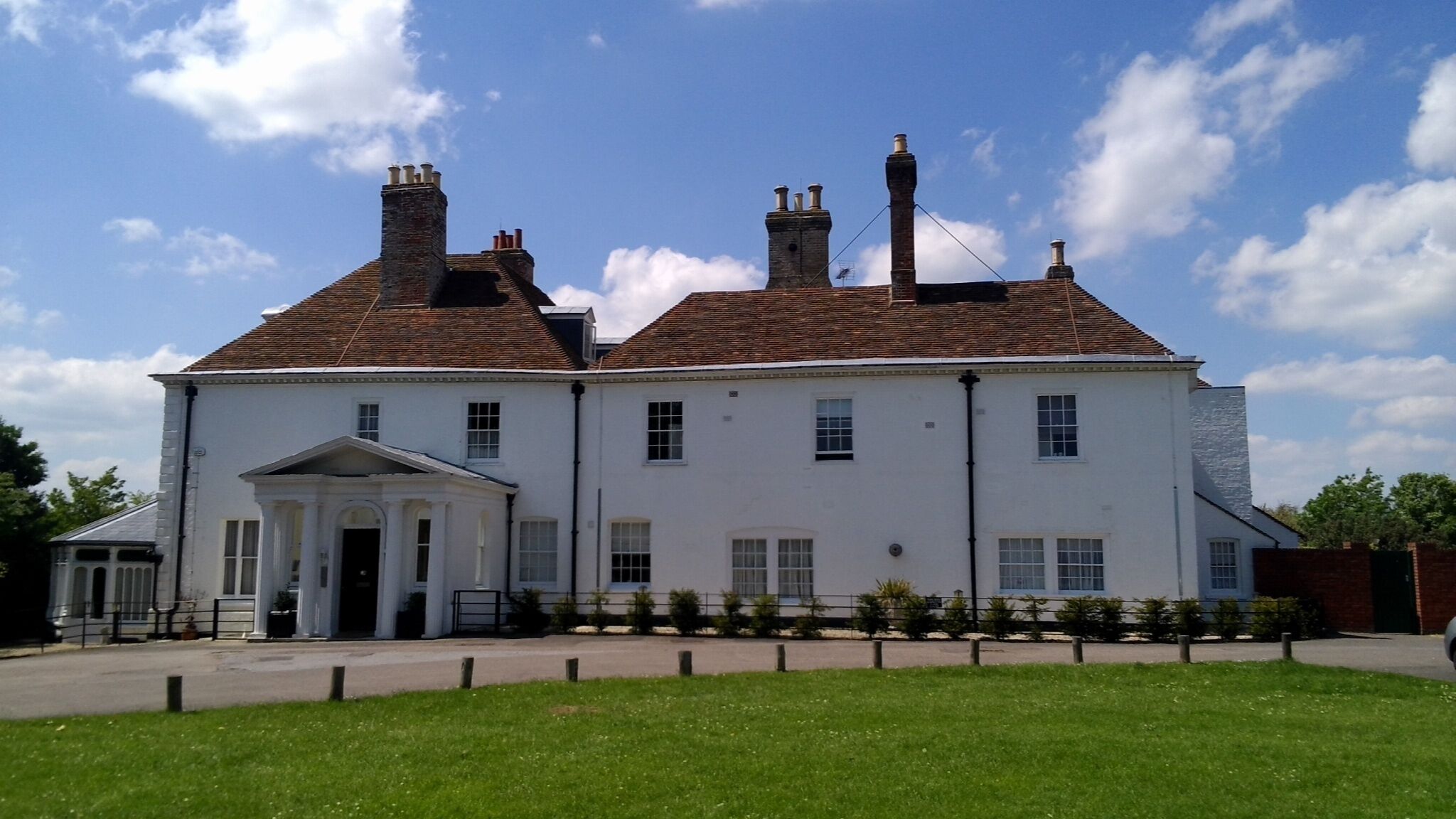A large white building with a central entrance, multiple chimneys, and a well-maintained lawn.