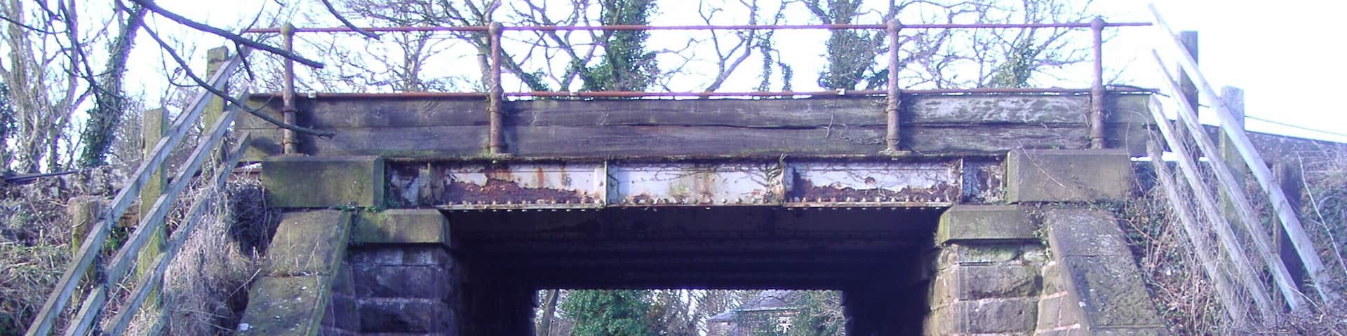 A stone bridge with metal railings and a paved road underneath.