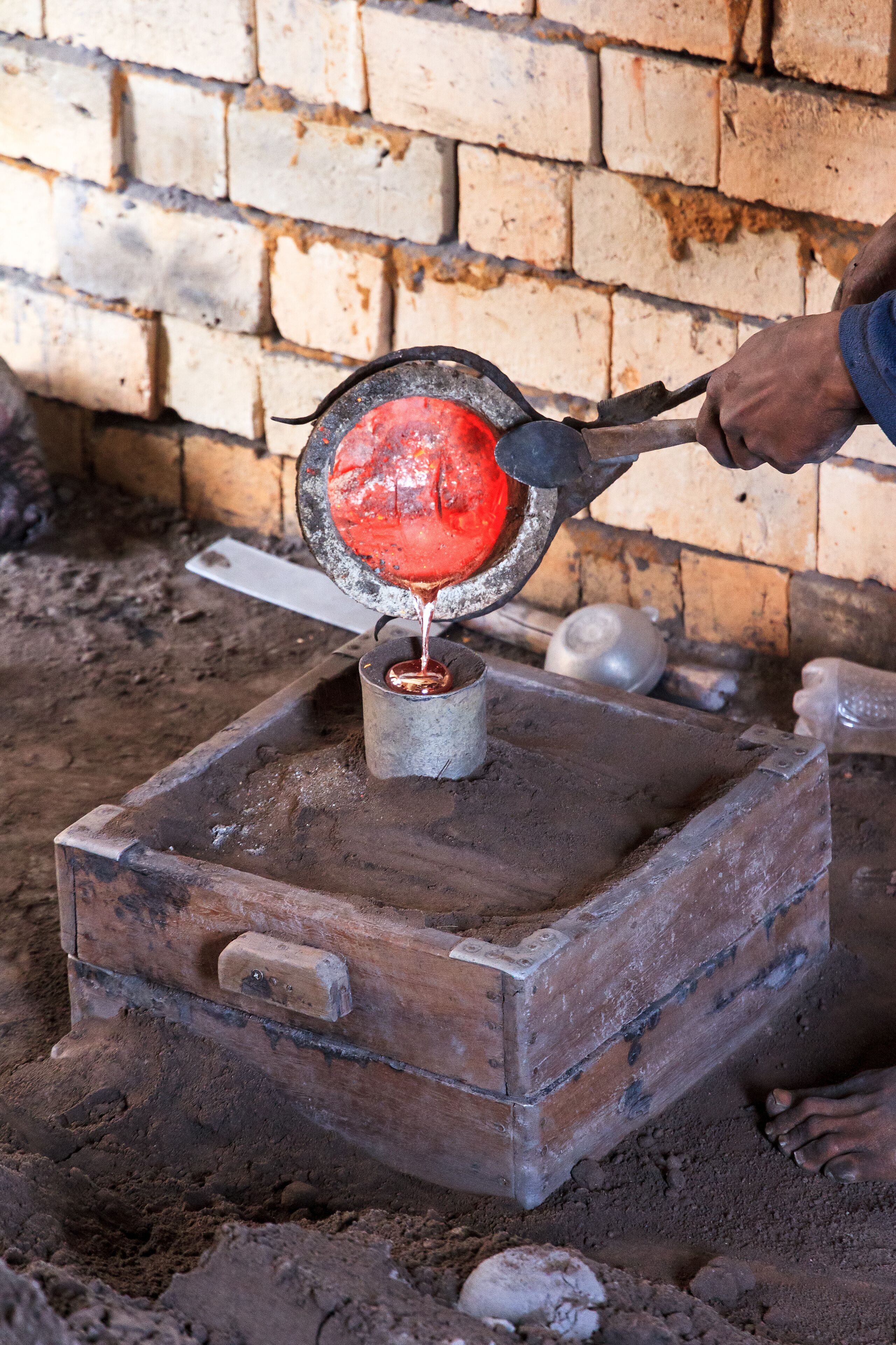 A person pouring molten metal into a mold on a brick structure.