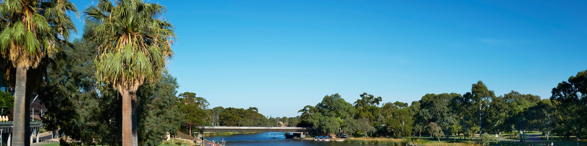 Un río con barcos, un puente y un parque con árboles y un sendero.