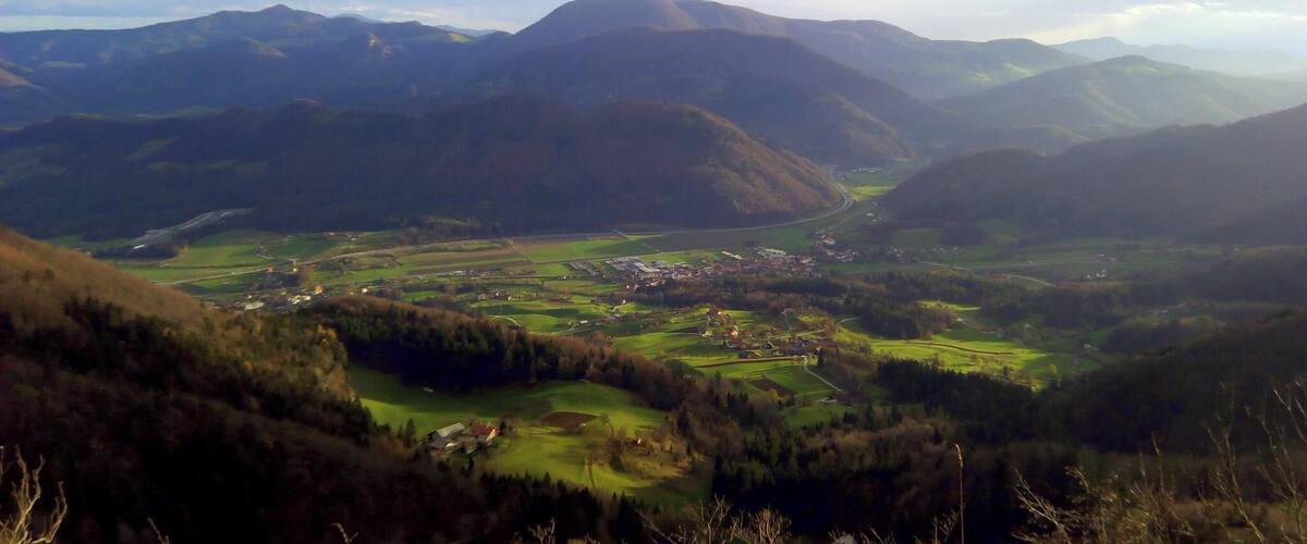 A valley with rolling hills, a small town, and distant mountains under a partly cloudy sky.